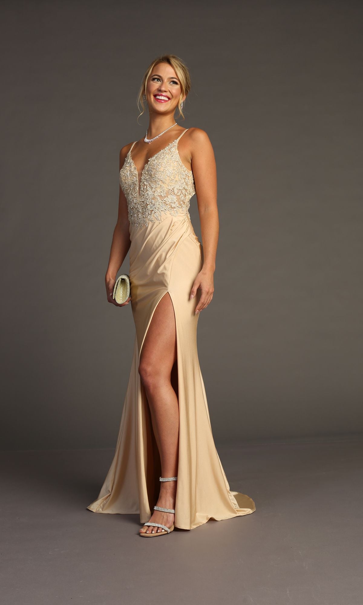 A woman in the Chicas YG5033 Lace-Bodice Slinky Long Prom Dress with a sleeveless lace bodice and side slit poses against a plain background, accessorized with strappy heels, a clutch, necklace, and earrings.